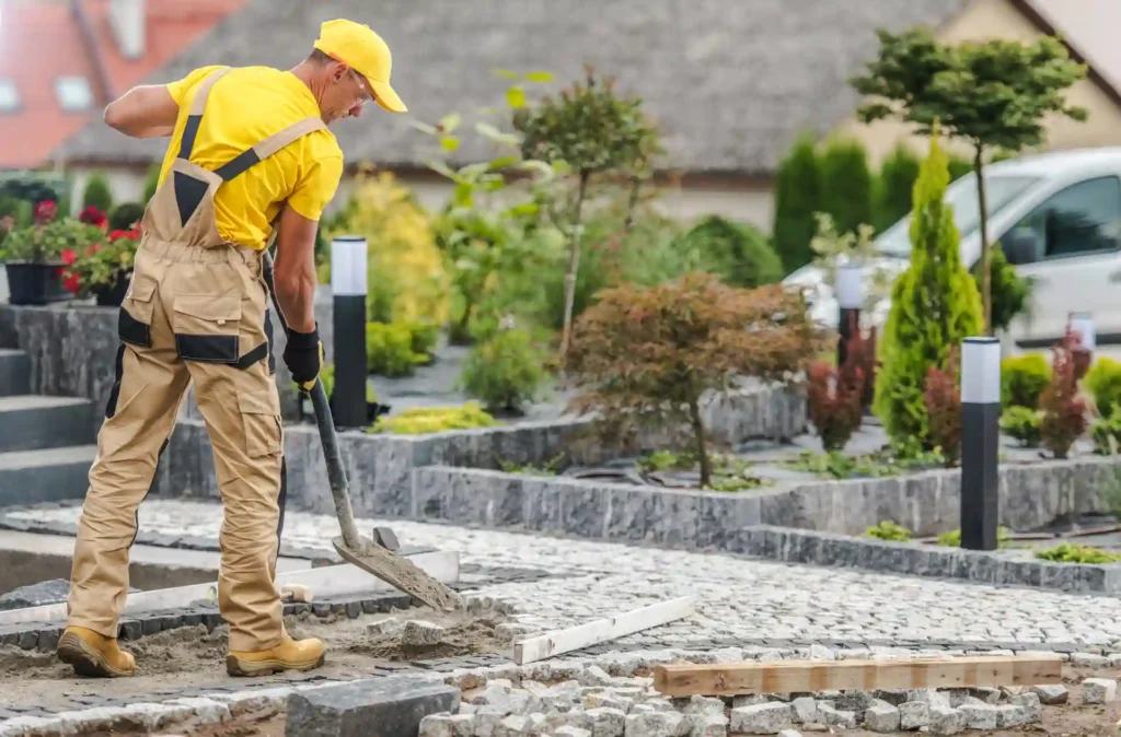 Worker repairing stone walkway, showing what does landscape maintenance include for hardscape care