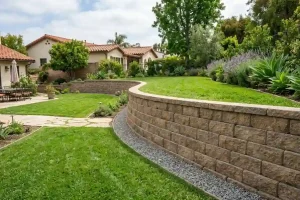 Curved concrete block retaining wall with gravel base and green lawn in a residential backyard showing proper retaining wall block installation