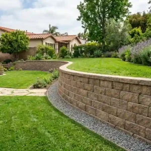 Curved concrete block retaining wall with gravel base and green lawn in a residential backyard showing proper retaining wall block installation